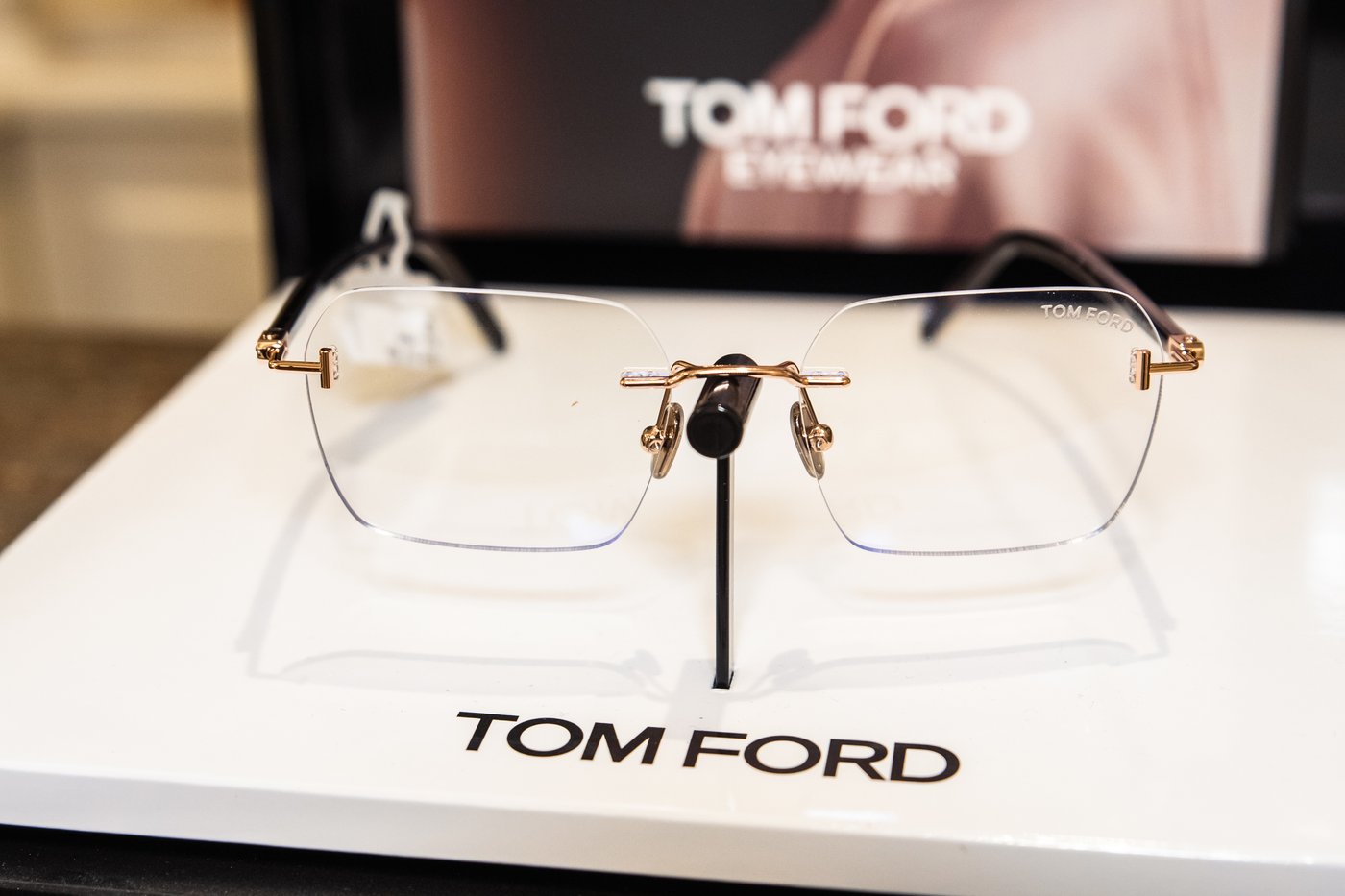 Occhiali da vista Tom Ford senza montatura con ponte dorato e aste nere su espositore bianco con logo del marchio